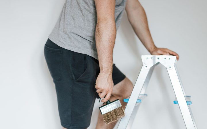 Side view of crop anonymous male decorator in casual clothes preparing to painting walls of light room while standing on step