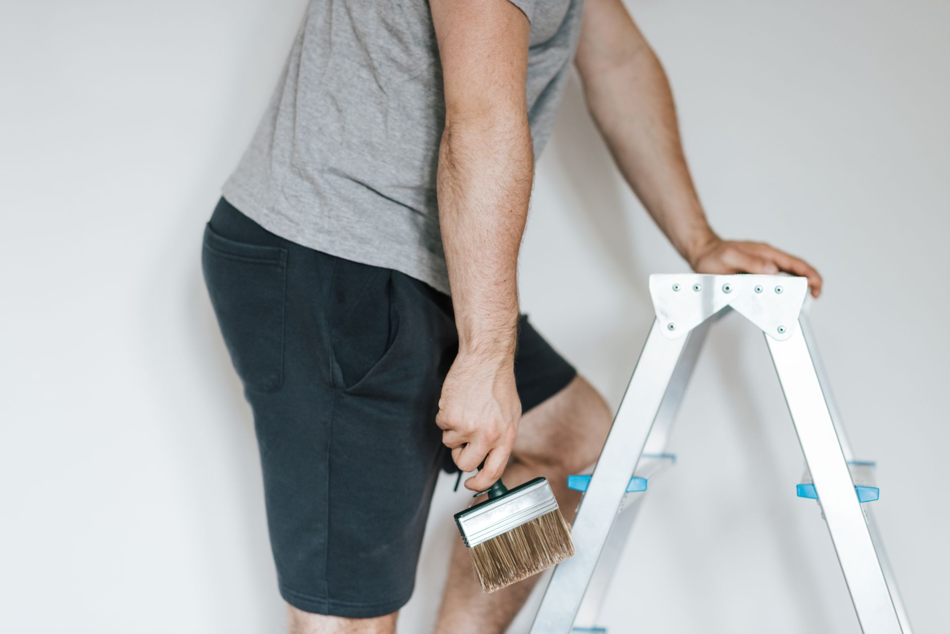 Side view of crop anonymous male decorator in casual clothes preparing to painting walls of light room while standing on step